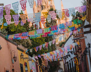 Angled image of the spires of Parroquia de San Miguel Arcángel rising behind a street fluttering with papel picado bunting.