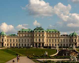 Visitors walk the grounds of the baroque Upper Belvedere Palace, with green copper octagonal, mansard, and domed roofs.
