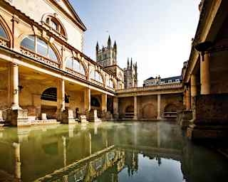 Open-air Roman bath surrounded by sandstone columns under blue skies