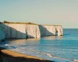The white cliffs of Botany Bay Beach at Broadstairs in Kent glow in the sun as the calm blue sea laps at the golden sands.