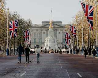 View down The Mall, lined with Union Jack flags, to Buckingham Palace, where crowds gather by the Queen Victoria Memorial.