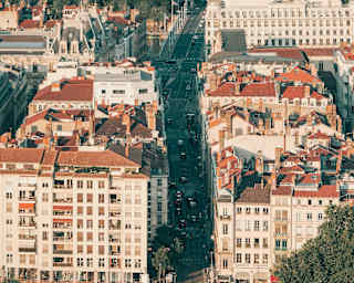 Aerial view of a Lyon bridge over the river Rhone with glimpses of a busy street beyond, shaded by tall buildings either side.
