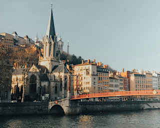 The red Passerelle Saint-Vincent bridge crosses the Saône, met on the south side by the grey-spired Église Saint-Georges de Lyon.