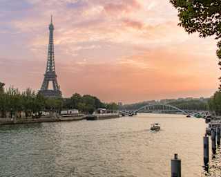 View from the Right Bank over the river Seine to the Left Bank, where the iconic Eiffel Tower rises against a plum sunset sky.