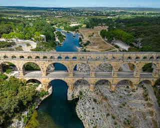Aerial view of the Roman-built Pont du Gard aqueduct, with three tiers of arches spanning the forest-edged Gardon River.