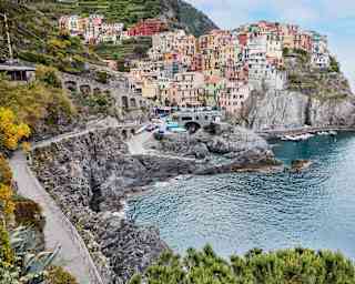 The tiny, picturesque Cinque Terre town of Manarola, with pastel buildings clinging to a rock above a small azure harbour.