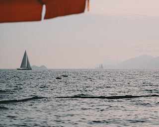 Burnt orange coloured parasol framing a view of a sailing boat at sunset