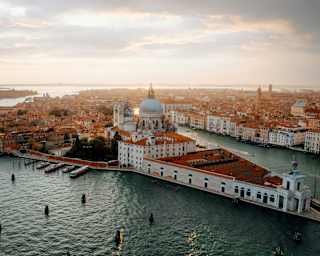 Stunning high-angle view over the Venice lagoon to Giudecca and the historic centre, terracotta roofs glowing in evening sun.