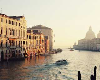 A boats cruises towards Basilica Santa Maria della Salute on the Grand Canal as morning sun glows on the waterfront buildings.
