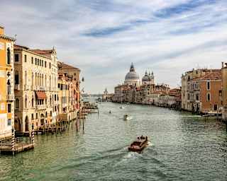 Boats cruise the greenish Grand Canal, flanked by sun-drenched Venetian houses, in a view capturing the Punta della Dogana.