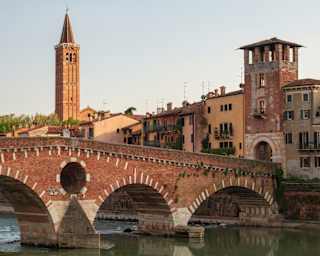 The red and white Ponte Pietra crosses Verona's Adige river, stopping at the stone archway flanked by riverside houses.