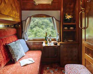 A book sits on the red banquette and a champagne bottle and two glasses wait on the window table in the cosy Pullman Cabin.
