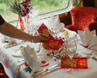A waiter places red and gold lucky money bags on a table in Malaya Dining Car, decorated and laid for a celebration meal.