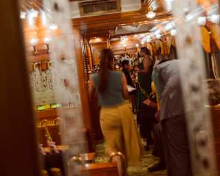 Tilted image of guests inside the piano bar car, illuminated by bright ceiling lamps, viewed through an etched glass panel.