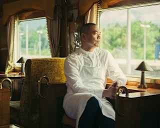 Chef André Chiang, in chef whites, sits at a wooden counter in the bronze-toned L'Oriental Car, gazing out of the window.