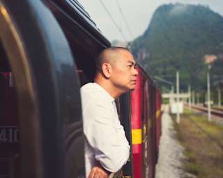 Chef André Chiang leans on the rails of an open-sided carriage, looking out, in an external shot along the side of the train.