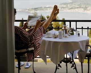 Lady in a red striped dress relaxing over breakfast with her bare feet rested on a balcony railing