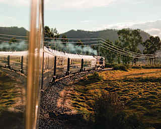 The train's shiny exterior reflects the front carriages as the track curves right around a bronze field, taken from a window.