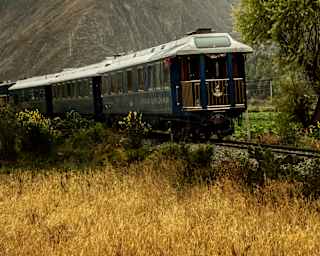 View of the train as it passes in front of a craggy mountain wrapped in cloud, with a glimpse of the Observation Car.