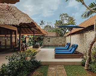 View across the terrace and garden, where two pairs of blue loungers recline under a matching parasol next to a plunge pool.