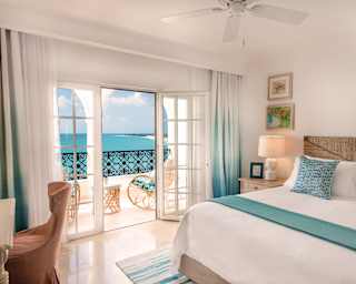 The Baie Orient Suite bedroom adds hints of teal to the crisp white of linen and walls to complement the dazzling ocean view.