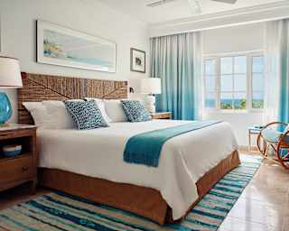 A rug striped in shades of blue and white softens the cool marble floor around a king bed topped with crisp white linens