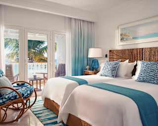 This twin room looks out through balcony doors to views of the sea and coconut palms. A cane rocking chair sits in the corner