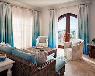 A dark rattan sofa with pale turquoise cushions looks out through arched patio doors to views of the sea and a private terrace