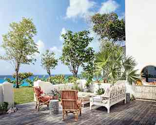 Cane furniture enjoys views over the low white walls of an enclosed decked garden, with views of the sea and lush gardens