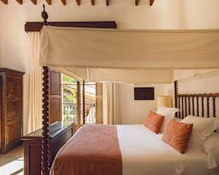 A large four-poster bed made with impossibly crisp white linens is topped with a terracotta throw and matching pillows