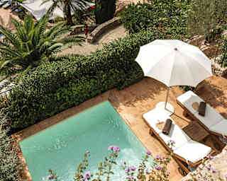 A birds-eye view shows a square of private pool and twin sun loungers beyond which the stone walls of ancient Deia unfold