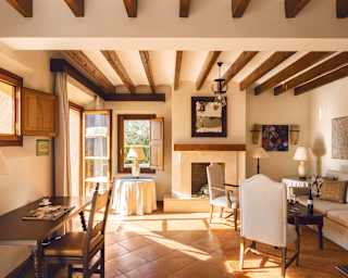 Sunlight sends paths of warmth across the tiled floor of a charming bedroom with exposed oak beams and four-poster bed