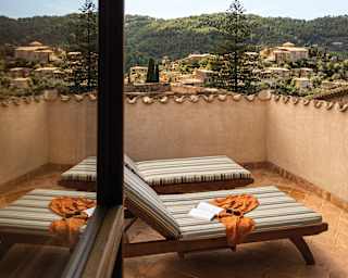 Teak sun loungers with striped cushions and a view over the hillside of Deià are reflected in the glass of an open window