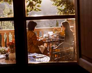 View from inside Miró restaurant to the terrace where two women sit in golden light at a table, enjoying incredible views.