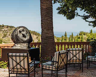 A carved, ball-like sculpture called Tête by Joan Miró sits on a plinth by a tree in the corner of a hill- and sea-view terrace.