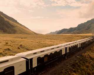 The Andean Explorer lets off steam as it heads through an Altiplano valley, with mountains either side, seen from just above.
