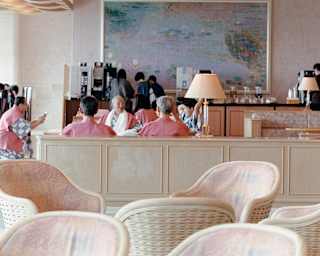 Five Japanese businessmen in pink tunics over grey-and-white tops relax at a table in a hotel, photographed by Cecy Young.