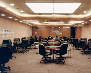 Ceiling spotlights illuminate a room with three rows of green-topped Mahjong tables in a hotel in Atami, taken by Cecy Young.