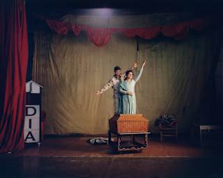 A woman and boy pose with a basket on a stage with a red curtain and broken 'India' sign at a magic convention in Bangalore.