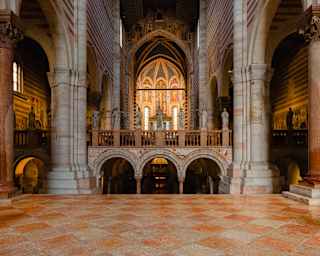 The interior of a Romanesque cathedral with stone arches, a tiled floor, and a stone rood screen featuring statues of saints.