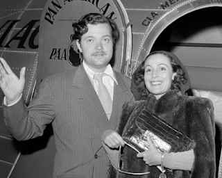 Black and white photo of American actor-director, Orson Welles and Mexican actress, Dolores del Rio, in an aeroplane doorway.