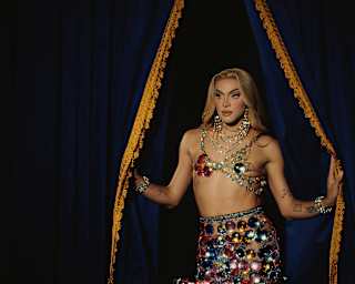 Brazilian drag queen, Pabllo Vittar poses by black velvet curtains in a beaded, upcycled glamour twin-set by Germanier.