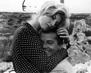 Monica Vitti, wearing a polka dot shirt, embraces Gabriele Ferzetti in a scene from the film L'Avventura, in black and white.