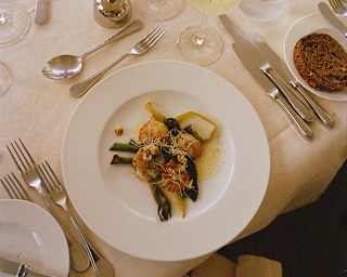 Looking down on a plate of king prawns, greens and buttery sauce at dinner on the Amaryllis, with wine, candles and cutlery.