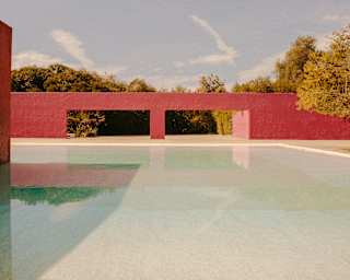View over a shallow pool to a red wall with two flat arches belonging to the Cuadra San Cristóbal by architect Luis Barragán.