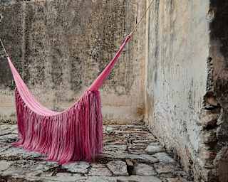 A sculptural hammock with sisal manes, based on a Mayan design, hangs in a stone courtyard, created by Fernando Laposse.