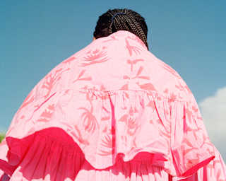 Low-angle image of a two-layered pink cape billowing out behind its wearer, seen from behind.