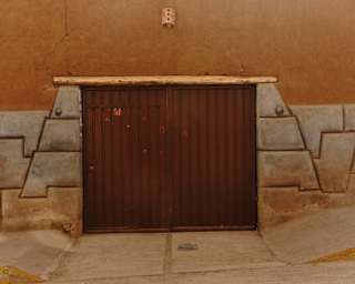 View of an old brown garage door set into an ochre-painted wall, surrounded by geometric-shaped stone bricks.
