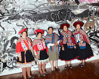 Five Peruvian women in bright woven shawls, four in montera hats, stand in front of large-scale ink artwork by Wu Jian'an.