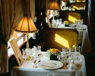 Gold light brushes the green velvet Etoile du Nord dining chairs, in a high-angle view over a laid tables with glowing lamps.